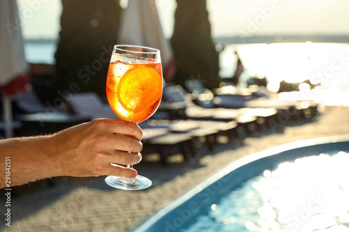 Man with glass of fresh summer cocktail near swimming pool outdoors, closeup. Space for text