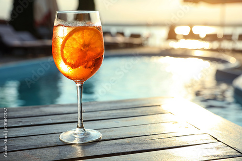 Carta da parati Glass of fresh summer cocktail on wooden table near swimming pool outdoors at sunset