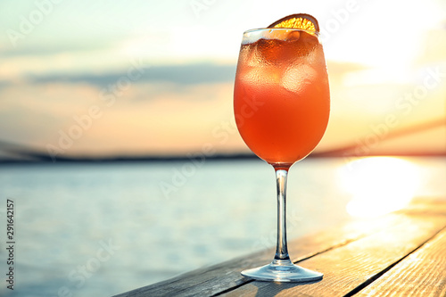 Sticker Glass of fresh summer cocktail on wooden table outdoors at sunset
