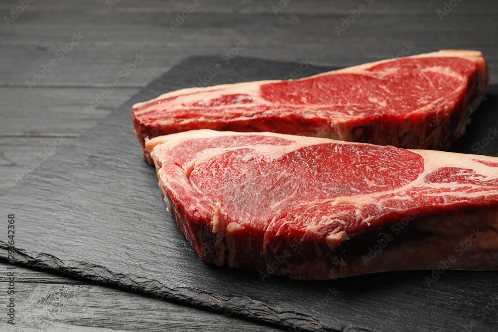Slate plate with fresh beef meat on black wooden table, closeup
