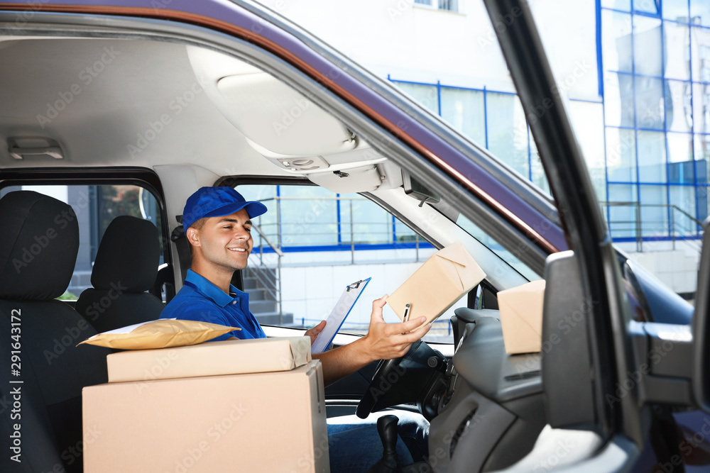 Young courier with clipboard and parcels in delivery car Young courier with clipboard and parcels in delivery car