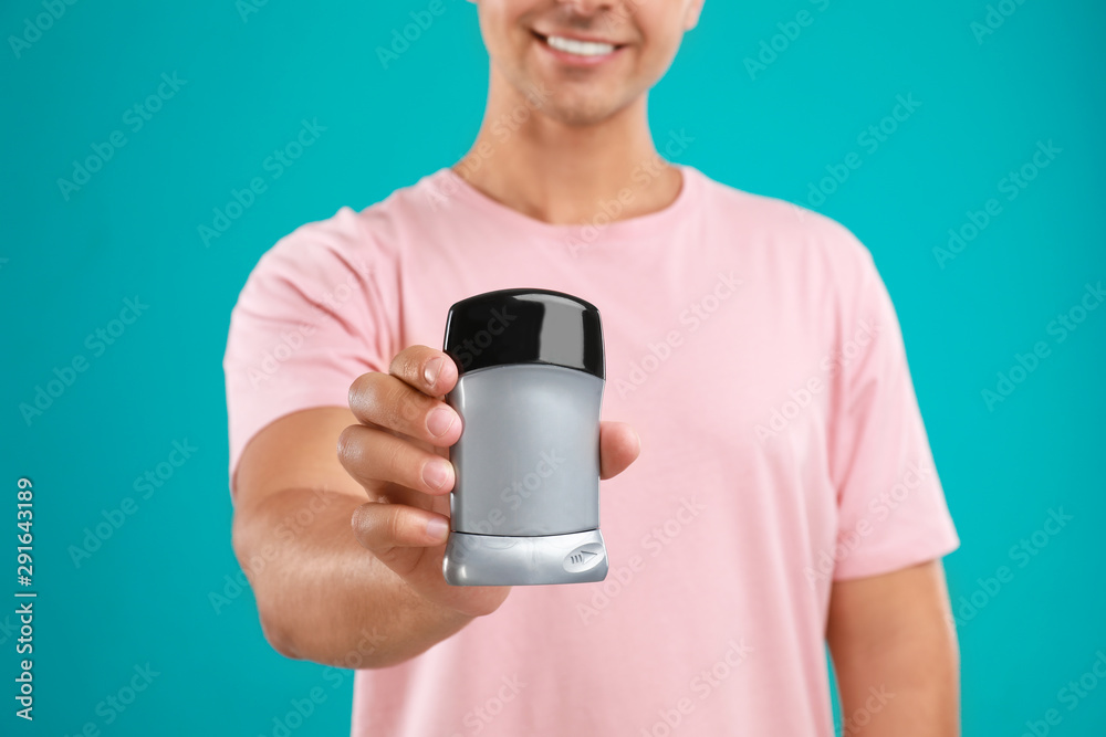 Young man holding deodorant on blue background, closeup. Mockup for design Young man holding deodorant on blue background, closeup. Mockup for design