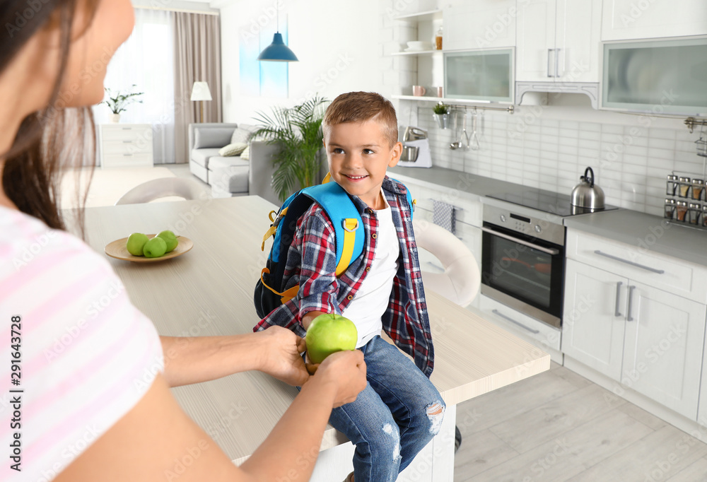 Happy mother giving apple to little child's with school bag in kitchen Happy mother giving apple to little child's with school bag in kitchen