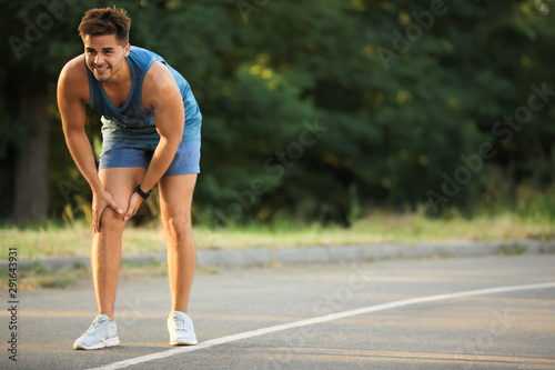 Young man in sportswear having knee problems in park