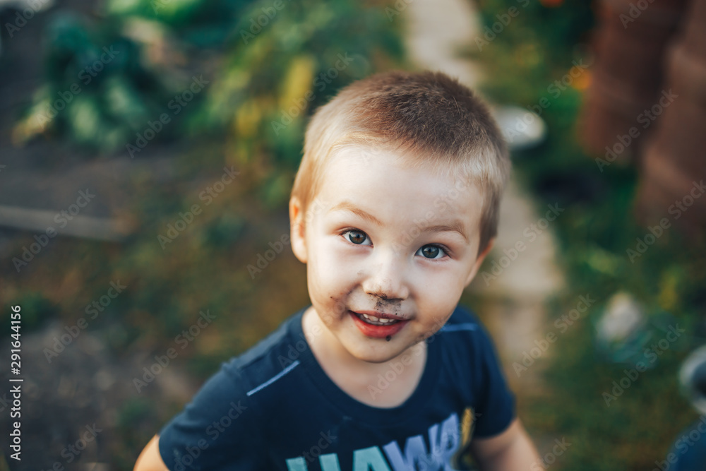 Blonde boy with disheveled hair smiling on a black couch after playing outside in the garden Blonde boy with disheveled hair smiling on a black couch after playing outside in the garden
