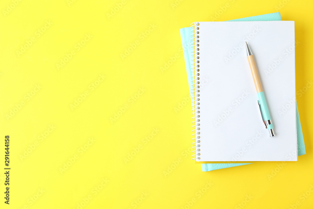 Notebooks and pen on yellow background, top view. Space for text Notebooks and pen on yellow background, top view. Space for text