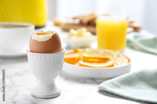 Cup with soft boiled egg on marble table, space for text. Healthy breakfast