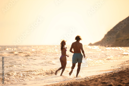 Young woman in bikini and her boyfriend having fun on beach at sunset. Lovely couple