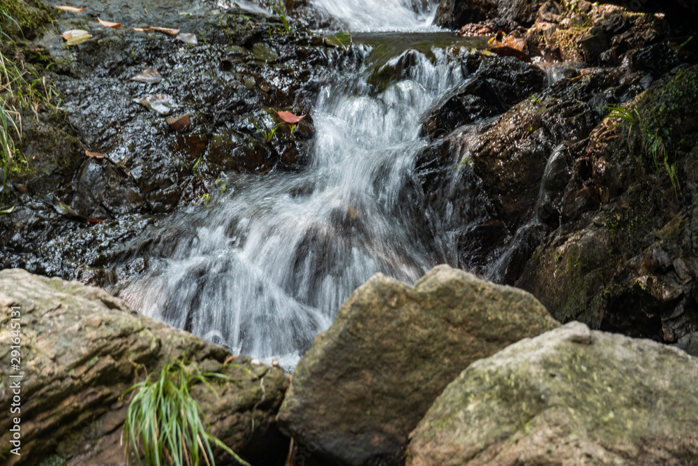 Naklejka premium rushing down waterfall blocked by big rocks inside park under the shade