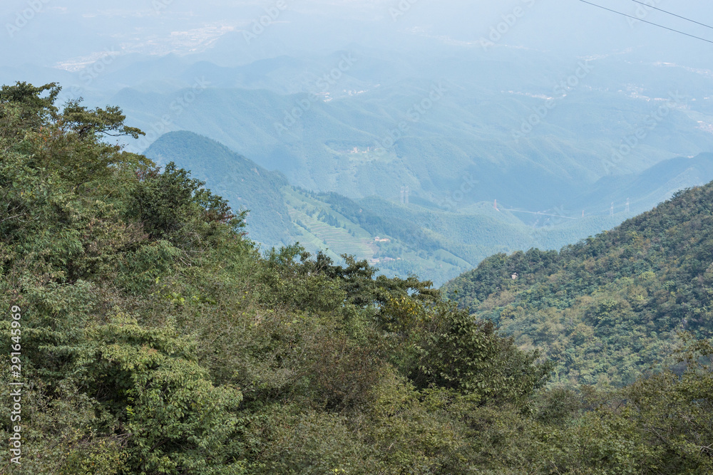 view from the top of a mountain throw the valley floor with forest covered slopes and small villages scatters around on the far end 