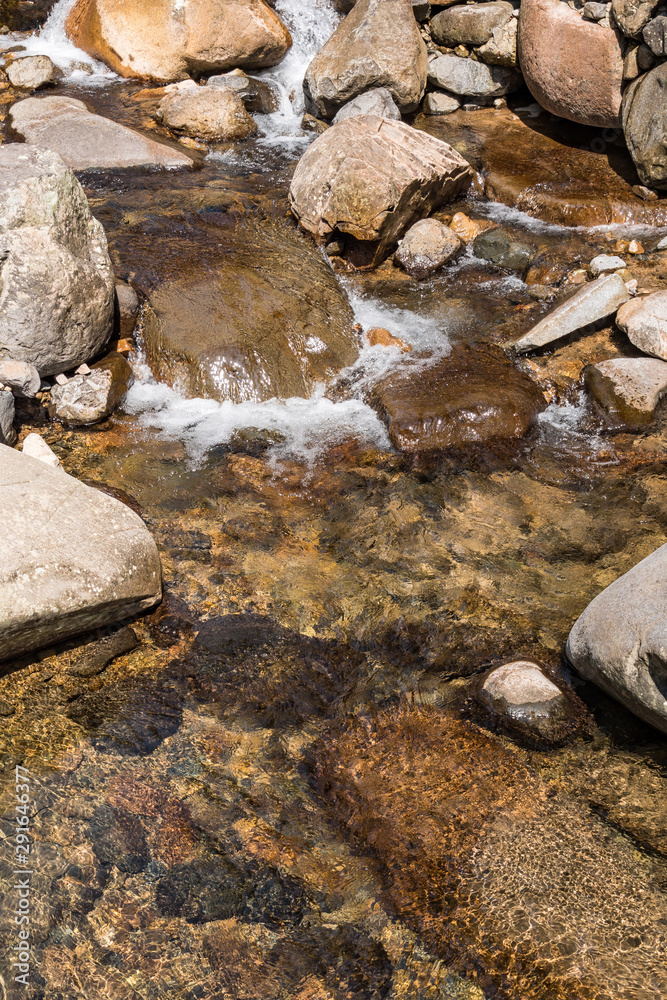 stream with crystal clear water flow through the rocky creek on a sunny day
