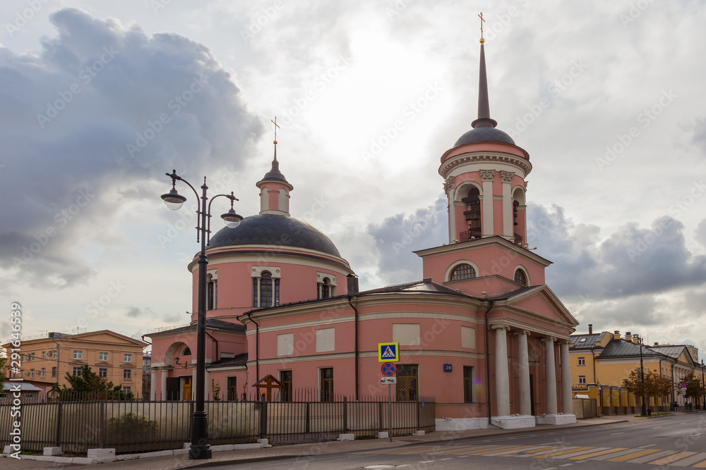 An old pink Orthodox church against a rainy sky. In the foreground is a street lamp.