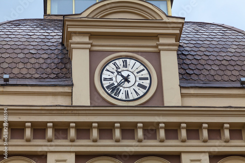 Clock above the entrance to the train station with a fragment of the roof, covered with brown metal tiles