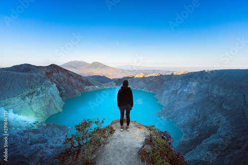 At sunrise girl stand on rock under volcano Kawah Ijen crater. Look at largest in world acid lake, sulphur mine. Popular travel destination, adventure hike on family vacation in Bali, Java, Indonesia photo