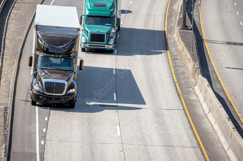 Big rigs semi trucks with semi trailers driving on merging road lines on wide highway
