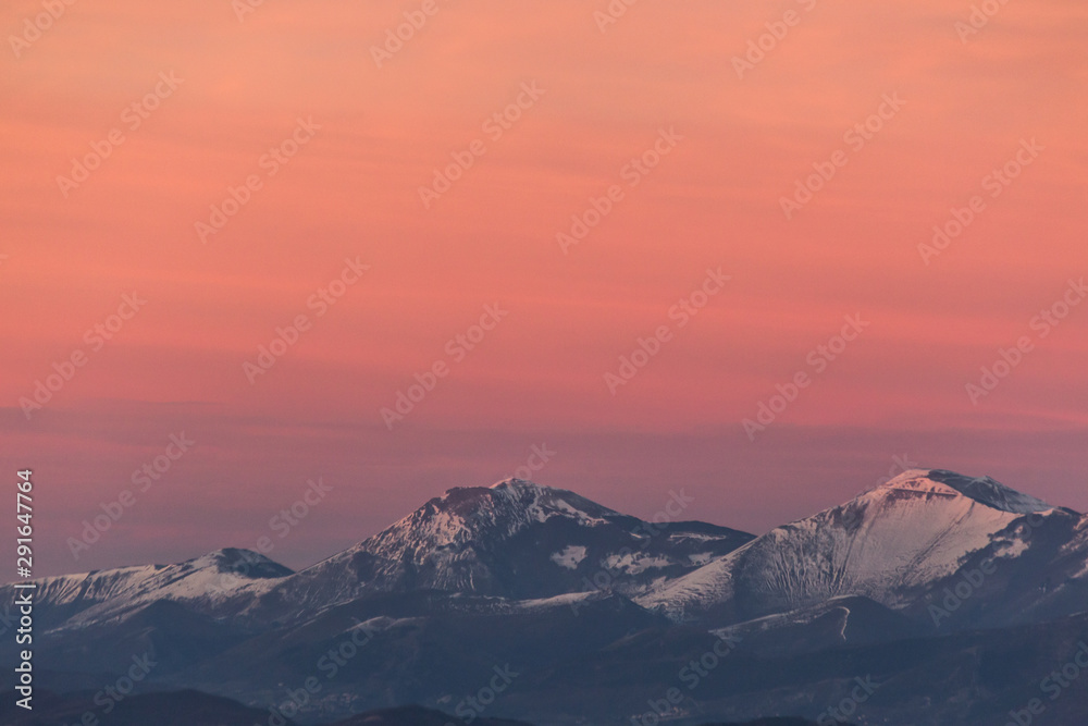 Mountain top covered by snow with a beautiful orange sky on the background