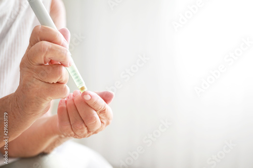 Diabetic woman taking blood sample with lancet pen at home, closeup