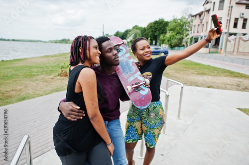 Group of three african american friends with skateboard making selfie on phone.