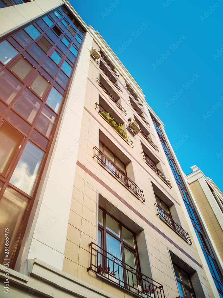Beige-brown facade of a multi-storey building in a classical style with a beautiful window decor. Housing concept, design of residential buildings.