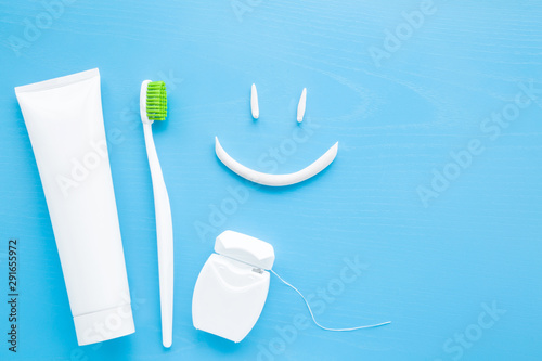Toothbrush with green bristles, white tube of toothpaste, dental floss on pastel blue background. Smiley face created from paste. Happy for healthy teeth concept.