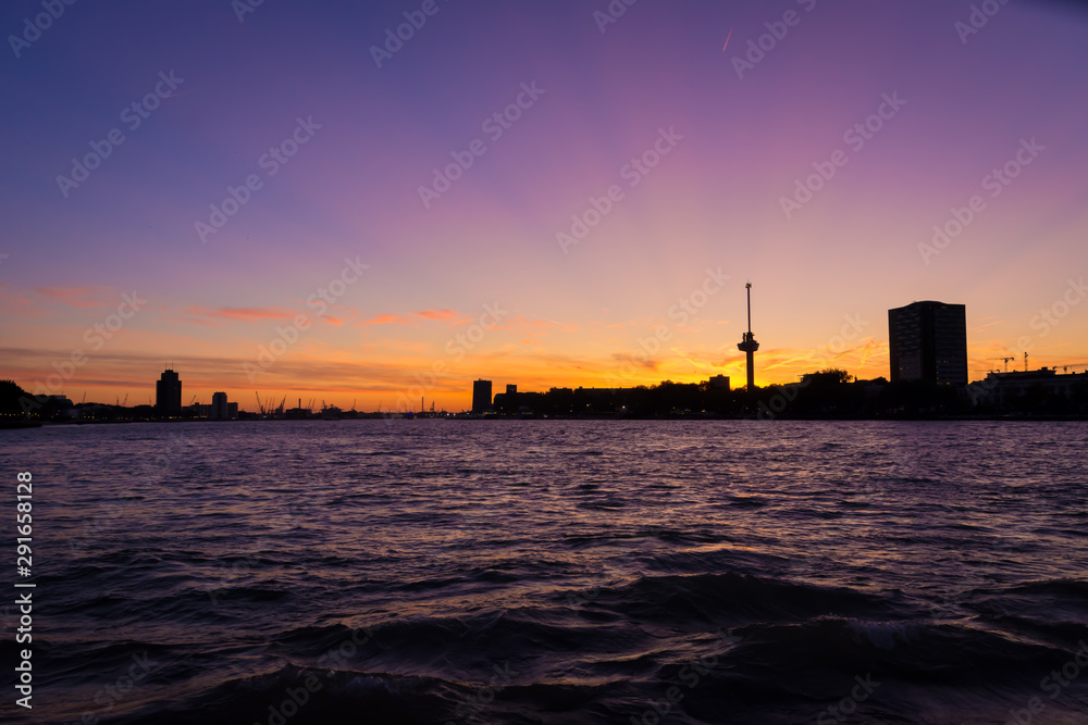 Rotterdam harbor at magenta colored sunset: view on the Euromast and Delfshaven area silhouette. Harbor cranes in the far distance. Picture taken from Wilhelminapier