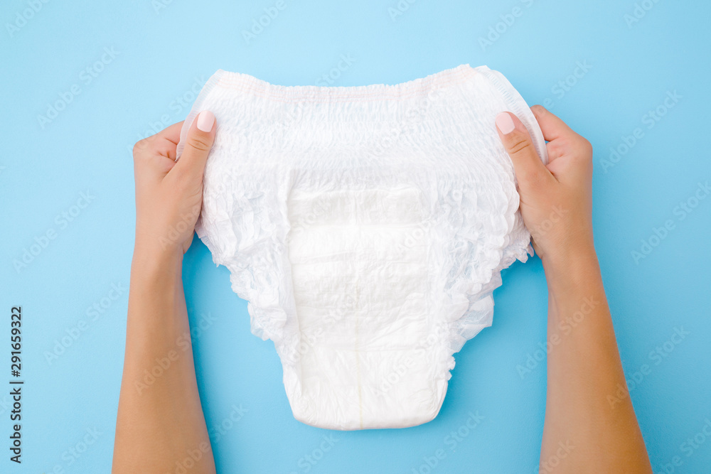 Woman hands holding white adult diaper on pastel blue background. Closeup. Point of view shot. Woman hands holding white adult diaper on pastel blue background. Closeup. Point of view shot.