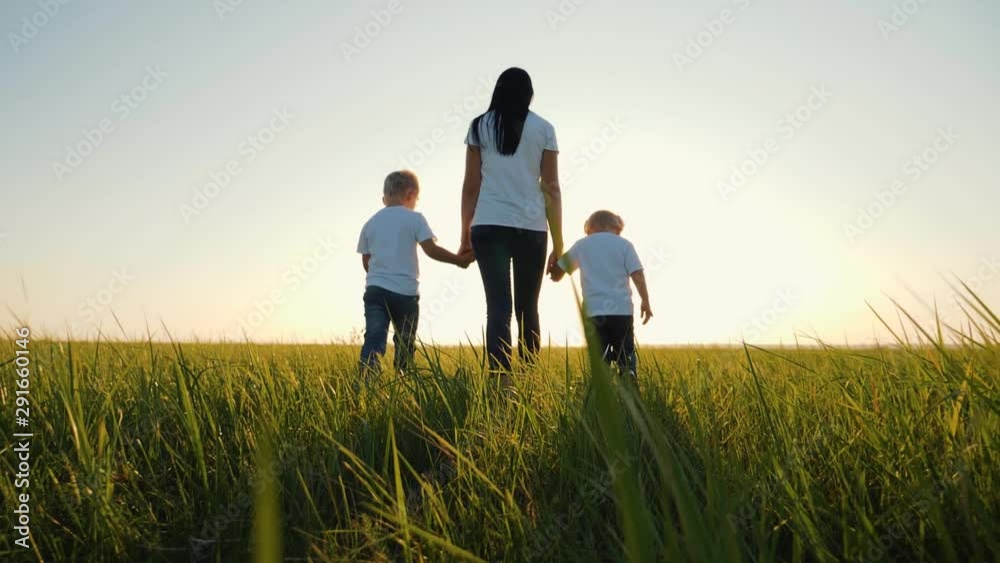 A happy family. Mom with children walks on a green field at sunset. Traveling and walking outdoors. The concept of happiness and health. Teamwork A happy family. Mom with children walks on a green field at sunset. Traveling and walking outdoors. The concept of happiness and health. Teamwork