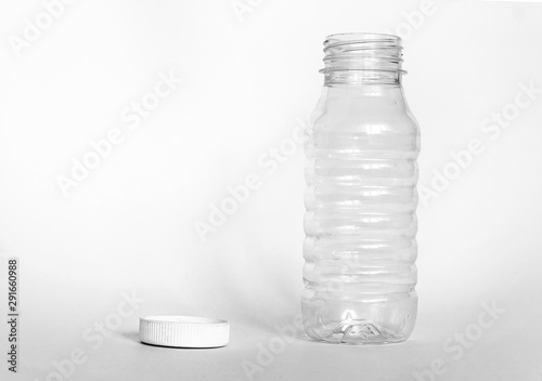 Fototapeta Naklejka Na Ścianę i Meble -  empty transparent open plastic bottle without cap, cap lies next to a white background, the concept of debris removal