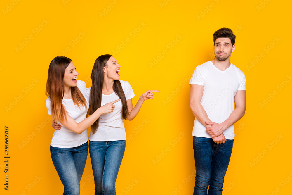 Portrait of confused person looking at funny girls teasing wearing white t-shirt denim jeans isolated over yellow background Portrait of confused person looking at funny girls teasing wearing white t-shirt denim jeans isolated over yellow background