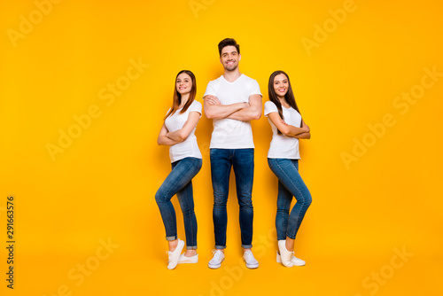 Full length photo of lovely hipsters crossing their arms smiling wearing white t-shirt denim jeans isolated over yellow background
