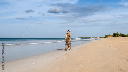 A woman on a Bicycle rides on the edge of the surf on the beach.