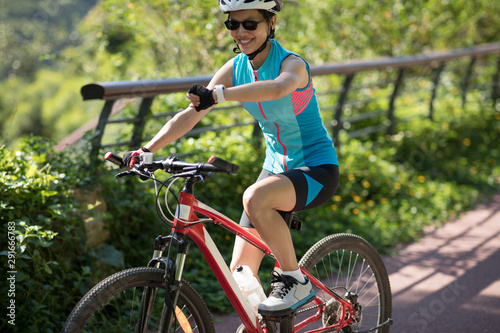 Woman riding on park bike path, looking at her smartwatch while riding bike on sunny day