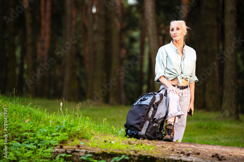 Portrait of Relaxing Senior Woman Posing with Smartphone and Tourist Backpack in Forest Outdoors.