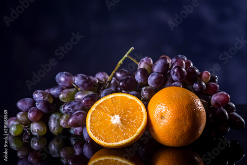 Two clusters of grapes and an orange are isolated on a black background.