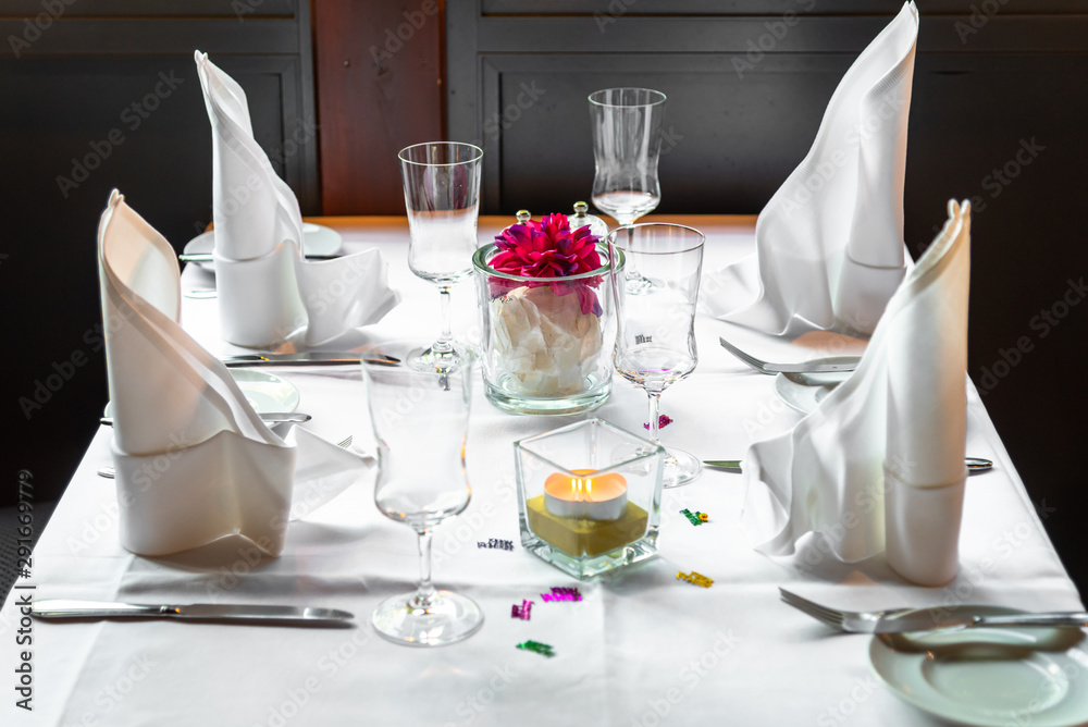 Table setting in a restaurant. Glass goblets, plates, candle, white napkins and decor on a white tablecloth