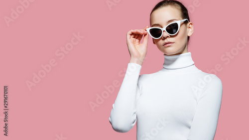 Fashion studio image of gorgeous elegant woman in white golf and sunglasses posing over pink wall.
