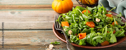 Paleo diet salad with arugula, baked pumpkin, hazelnut and sesame seeds on brown plate. Healthy food concept with copy space. Banner.