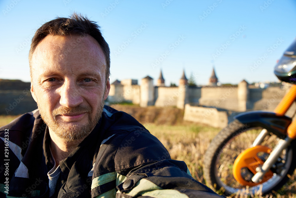 Male biker traveler makes selfie photo with a motorcycle on the background of the castle.