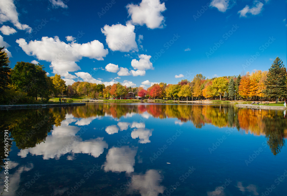 Obraz premium Autumn colorful trees and cotton clouds reflecting on Beaver Lake, Mount Royal, Montreal, Quebec, Canada