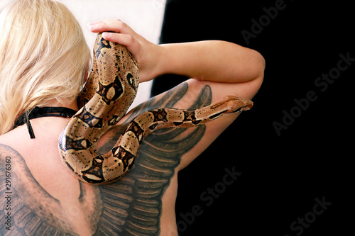 Snake on female shoulder and hand, part woman naked body. Non poisonous Boa constrictor species of snake slithering and crawling per woman hand, shoulder. Exotic tropical cold blooded reptile animal.