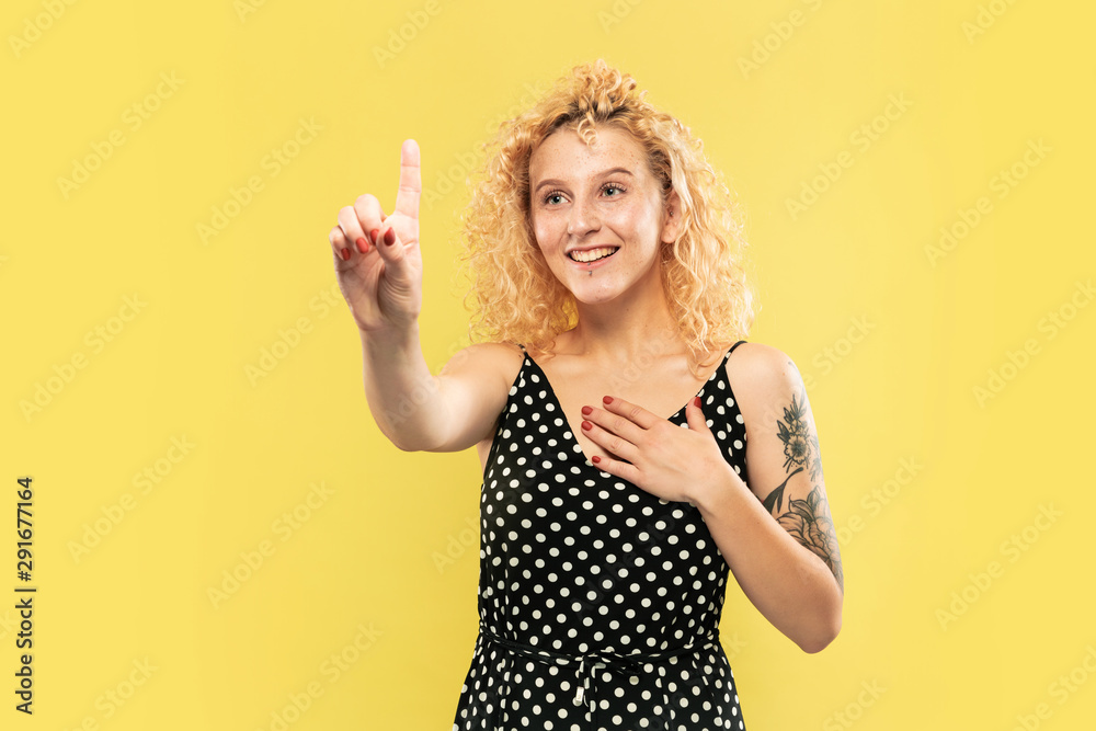 Caucasian young woman's half-length portrait on yellow studio background. Beautiful female model in black dress. Concept of human emotions, facial expression. Touching an empty search bar, smiling. Caucasian young woman's half-length portrait on yellow studio background. Beautiful female model in black dress. Concept of human emotions, facial expression. Touching an empty search bar, smiling.