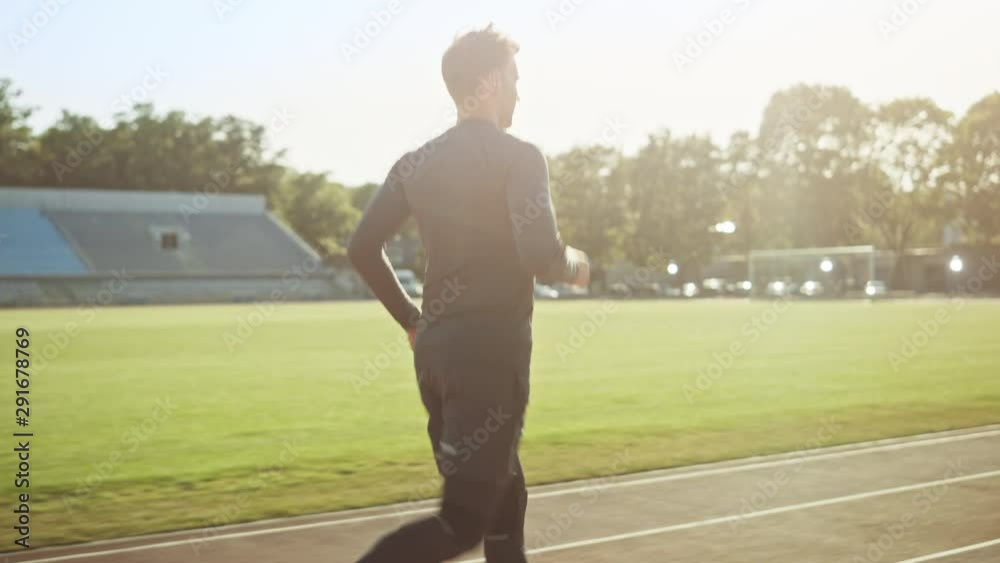 Athletic Fit Man in Grey Shirt and Shorts Jogging in the Stadium. He is Running Comfortably on a Warm Summer Afternoon. Athlete Doing His Routine Sports Practice. Tracking Shot. Athletic Fit Man in Grey Shirt and Shorts Jogging in the Stadium. He is Running Comfortably on a Warm Summer Afternoon. Athlete Doing His Routine Sports Practice. Tracking Shot.