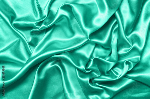 Close up of ripples on silk fabric. Satin textile background. Green color. Top view. Color of the year 2020