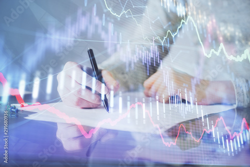 Hand taking notes in notepad. Forex chart holograms in front. Concept of research. Multi exposure