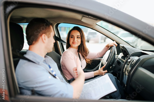 Male auto instructor takes exam in young woman. Positive happy model look at guy and smile. Driving car alone and careful. Guy talks to her. Passing exam. © estradaanton