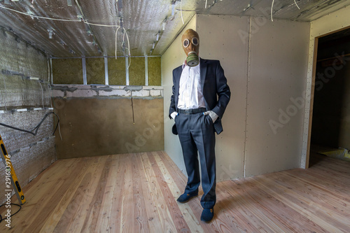 Strange man in businessman suit and gas protection mask inside a room under renovation works.