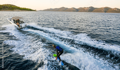 Fotografija Aerial photo of man practicing wakeboarding towed by speed boat in deep blue sea