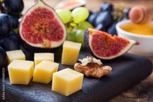 Cheese cubes, fresh fruit figs grapes Honey walnut on wooden chopping Board. Selective focus. Close up.