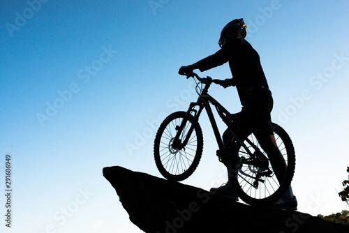 Silhouette of the athlete standing on the rock with bicycle