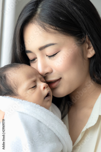 Close up asian young mother hugging and kissing her cute newborn baby. Wife and mother's day concept.